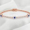 Rose gold sapphire and diamond bracelet featuring centered floral cluster design on white satin background