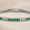 White gold green tsavorite and diamond channel-set tennis bracelet on neutral fabric background