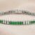 White gold green tsavorite and diamond channel-set tennis bracelet on neutral fabric background