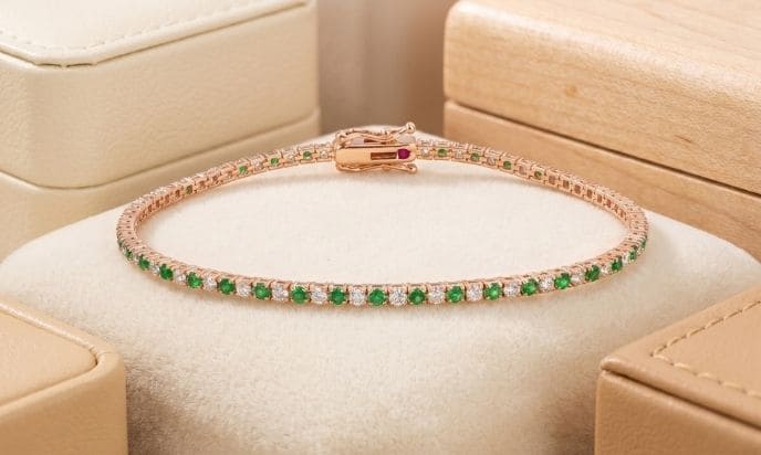 Rose gold natural diamond and emerald tennis bracelet displayed in luxury jewelry setting