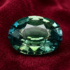 Natural oval blue green sapphire gemstone on red velvet fabric