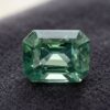 Natural emerald cut blue green sapphire gemstone on dark fabric