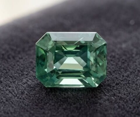 Natural emerald cut blue green sapphire gemstone on dark fabric