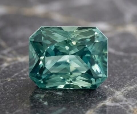 Natural blue green sapphire gemstone on dark stone surface