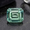Natural emerald cut blue green sapphire gemstone on dark stone surface