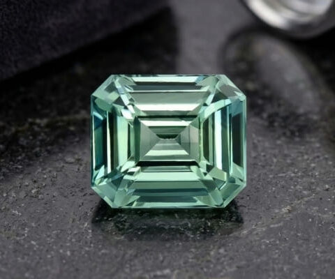 Natural emerald cut blue green sapphire gemstone on dark stone surface