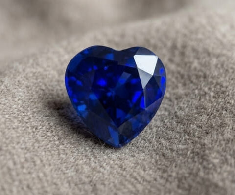 Natural blue sapphire heart shaped gemstone with deep blue color on soft fabric background