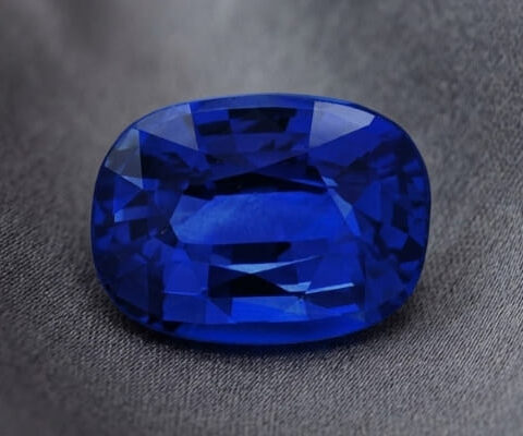 Natural blue sapphire gemstone with GIA report showing oval cut and deep blue color on fabric background
