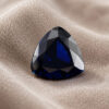Natural blue sapphire gemstone with triangular cut displayed on soft beige fabric background