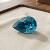 Natural pear shaped blue zircon gemstone on cream jewelry display