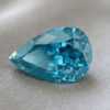 Natural pear shaped blue zircon gemstone on soft grey fabric