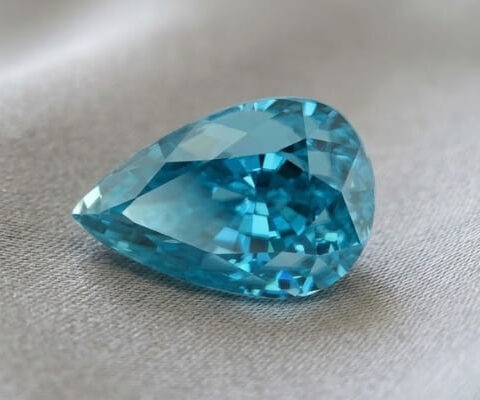 Natural pear shaped blue zircon gemstone on soft grey fabric