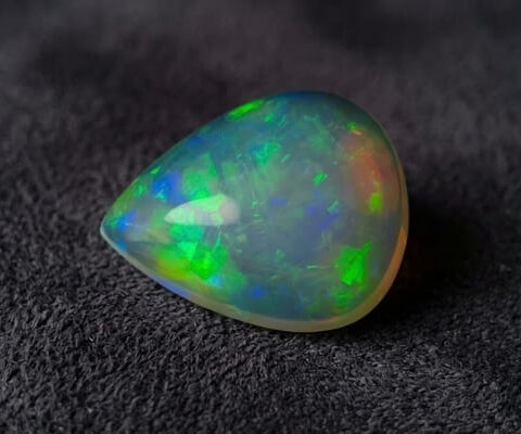 Natural pear shaped Brazilian opal gemstone on dark textured fabric