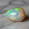 Natural pear shaped Brazilian opal gemstone on light stone surface