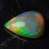 Natural pear shaped Brazilian opal gemstone on black stone surface