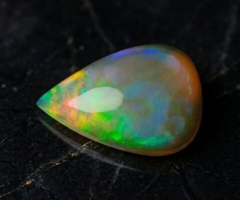 Natural pear shaped Brazilian opal gemstone on black stone surface
