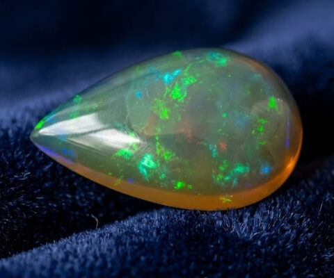 Natural pear shaped Brazilian opal gemstone on deep blue velvet fabric