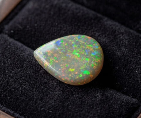 Natural pear shaped Brazilian opal gemstone on black velvet jewelry display