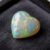 Natural heart shaped Brazilian opal gemstone on dark grey jewelry display