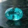 Natural oval Brazilian Paraiba tourmaline gemstone on dark green stone surface