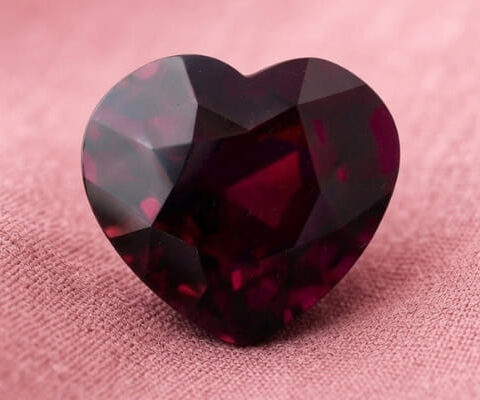 Natural heart shaped garnet gemstone on soft pink fabric