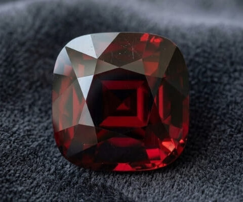 Natural cushion cut garnet gemstone on dark grey fabric