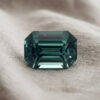 Natural emerald cut green blue sapphire gemstone on soft grey fabric