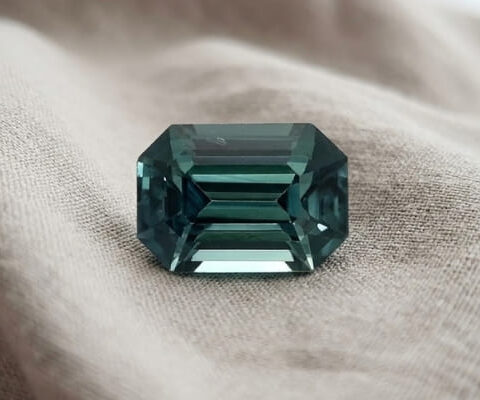 Natural emerald cut green blue sapphire gemstone on soft grey fabric