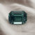 Natural emerald cut green blue sapphire gemstone on soft grey fabric