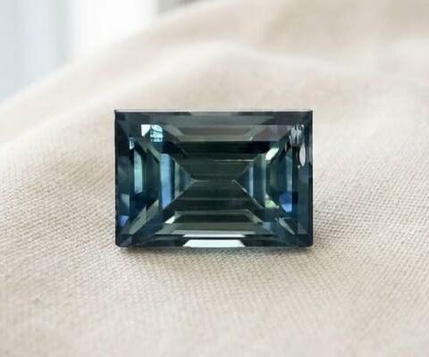 Natural emerald cut green blue sapphire gemstone on soft cream fabric