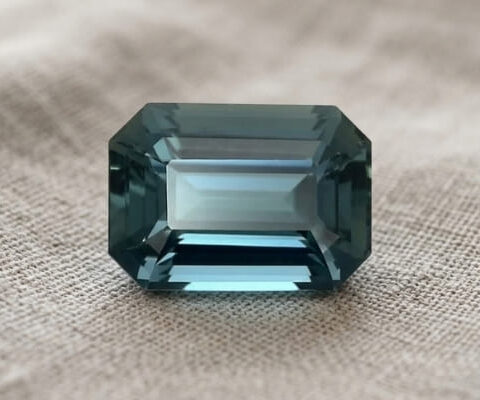 Natural emerald cut green blue sapphire gemstone on soft beige fabric