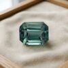 Natural emerald cut green blue sapphire gemstone on cream jewelry display
