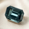 Natural emerald cut green blue sapphire gemstone on soft cream fabric