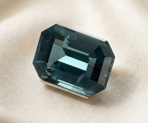 Natural emerald cut green blue sapphire gemstone on soft cream fabric