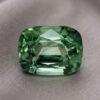 Natural cushion cut green sapphire gemstone on soft grey fabric