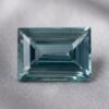 Natural emerald cut green sapphire gemstone on soft grey fabric