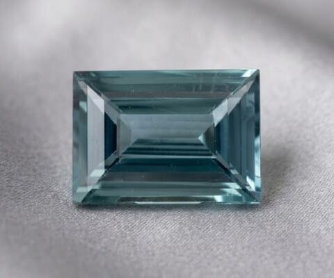Natural emerald cut green sapphire gemstone on soft grey fabric