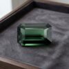 Natural emerald cut green sapphire gemstone on dark grey jewelry display