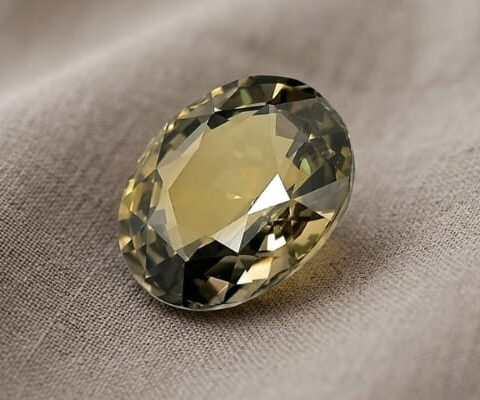 Natural oval green sapphire gemstone on soft taupe fabric