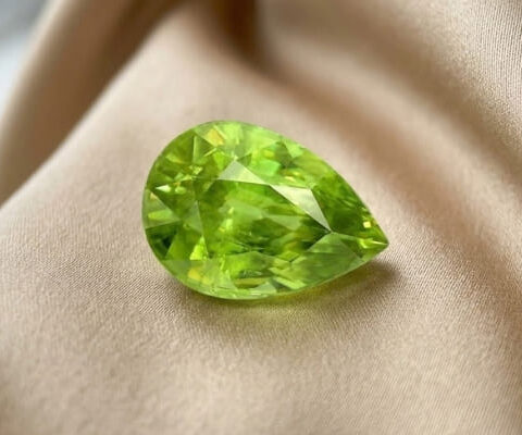 Natural pear shaped green sphene gemstone on soft beige fabric