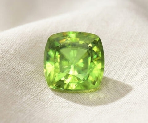 Natural cushion cut green sphene gemstone on soft cream fabric