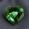 Natural heart shaped green tourmaline gemstone on dark grey fabric