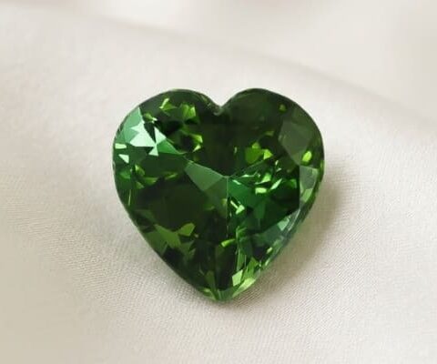 Natural heart shaped green tourmaline gemstone on soft cream fabric