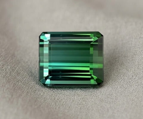Natural emerald cut green tourmaline gemstone on soft grey fabric