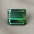 Natural emerald cut green tourmaline gemstone on soft grey fabric