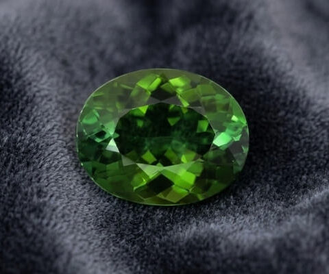 Natural oval green tourmaline gemstone on dark grey fabric