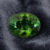 Natural oval green tourmaline gemstone on dark grey fabric