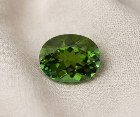 Natural oval green tourmaline gemstone on soft cream fabric