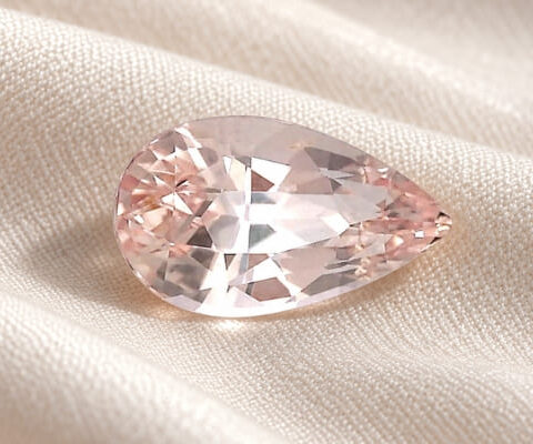 Natural pear-cut peach sapphire gemstone on soft ivory fabric