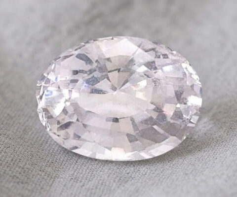 Natural oval-cut light peach sapphire gemstone on soft grey fabric